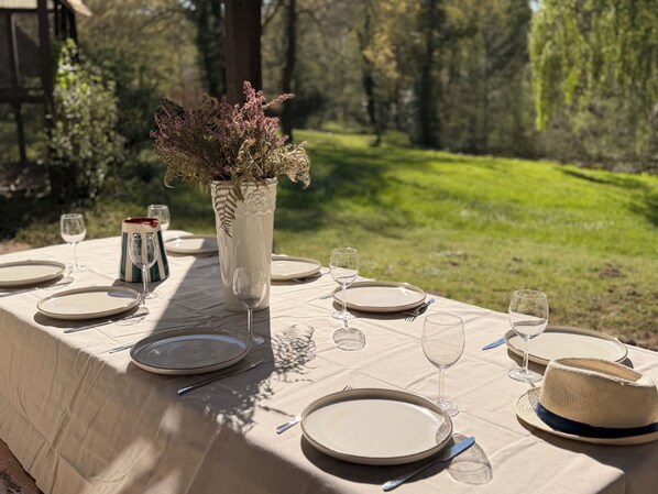 An outdoor dining table set with plates, cutlery, and a vase with dried flowers.