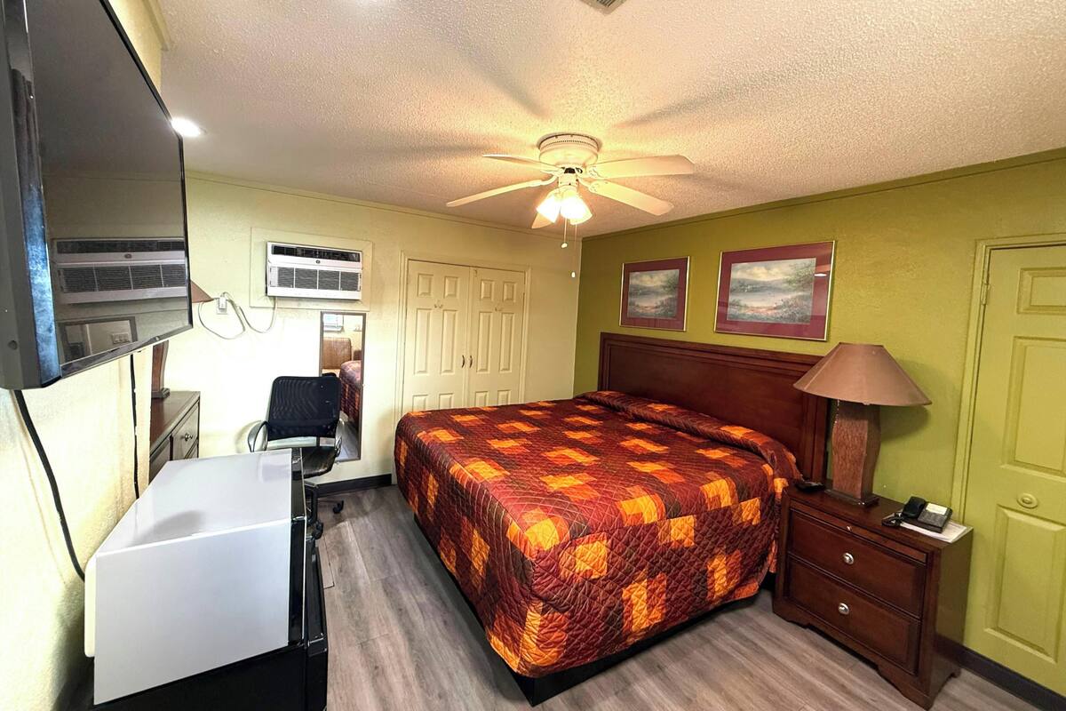 Een slaapkamer met een bed, bureau, stoel en een plafondventilator.