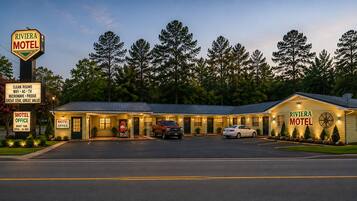 A motel with a signboard, two motel offices, a parking lot, and a building with a sign.