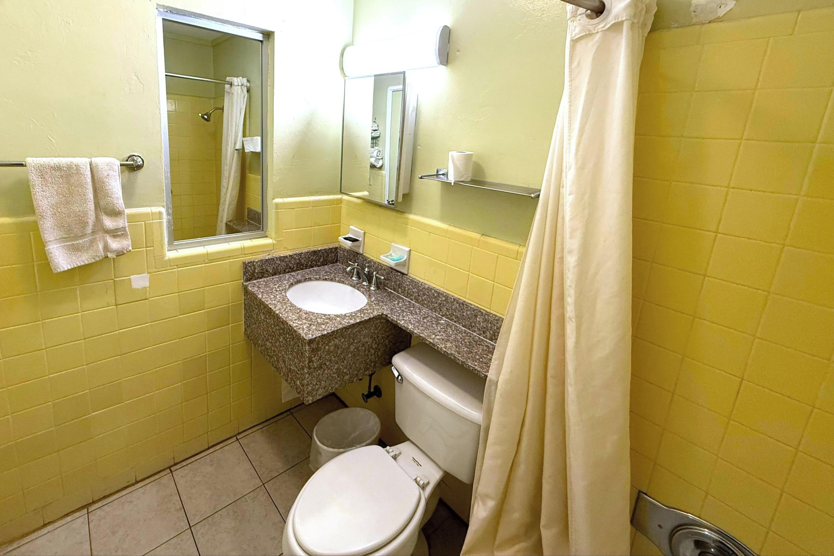 A bathroom with yellow walls, a white toilet, a sink with a mirror above it, and a shower curtain.