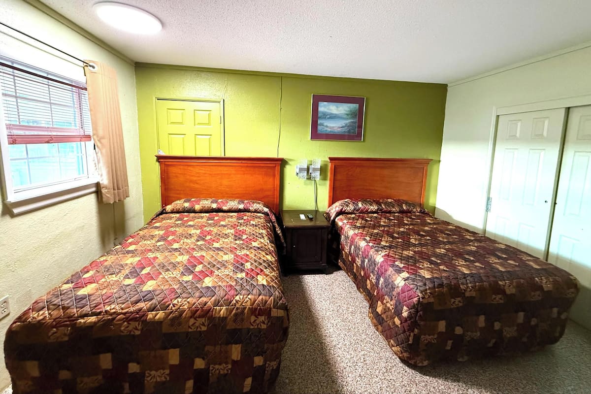 Een kamer met twee bedden, een raam met zonwering, een deur en een foto aan de muur.