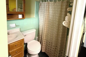 A bathroom with a toilet, sink, wooden cabinet, and a shower curtain. - Riviera Motel Elba Near Enterprise US 84 (Elba)