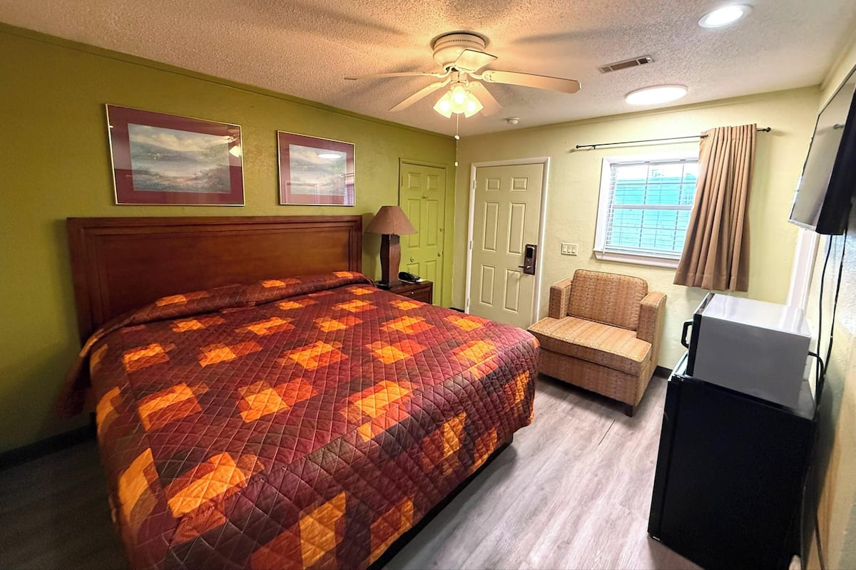 Een kamer met een bed, een stoel, een televisie en een plafondventilator.