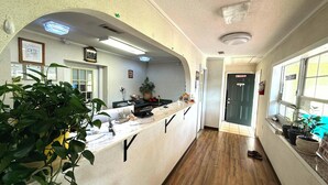 A reception area with a counter, potted plants, a clock, and a door with a 'No Smoking' sign. - Riviera Motel Elba Near Enterprise US 84 (Elba)