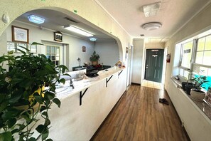 A reception area with a counter, potted plants, a clock, and a door with a 'No Smoking' sign. - Riviera Motel Elba Near Enterprise US 84 (Elba)