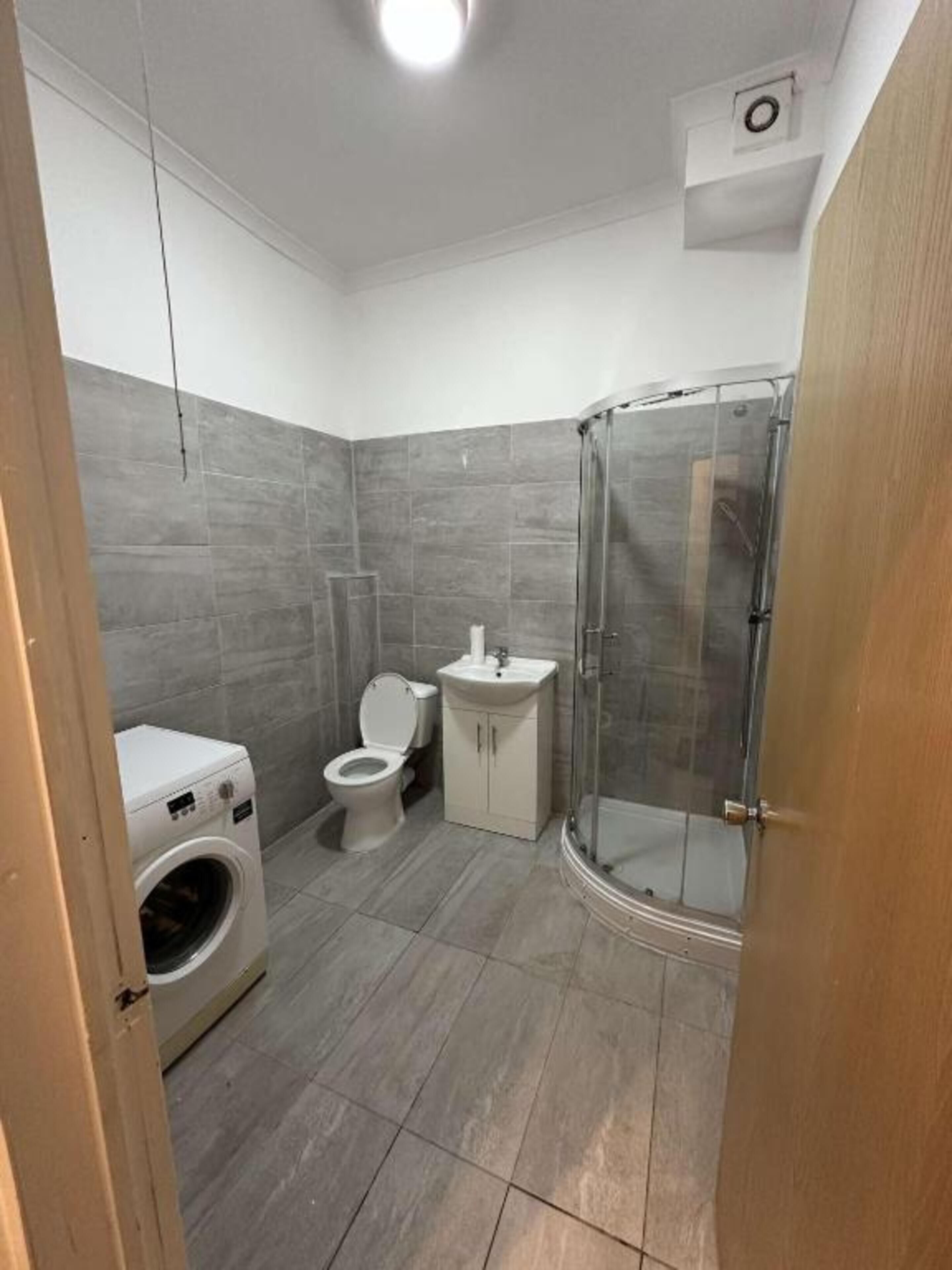 A bathroom with a shower, toilet, washing machine, and sink.