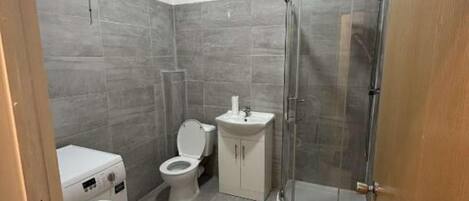 Et badeværelse med brusebad, toilet, vaskemaskine og håndvask.