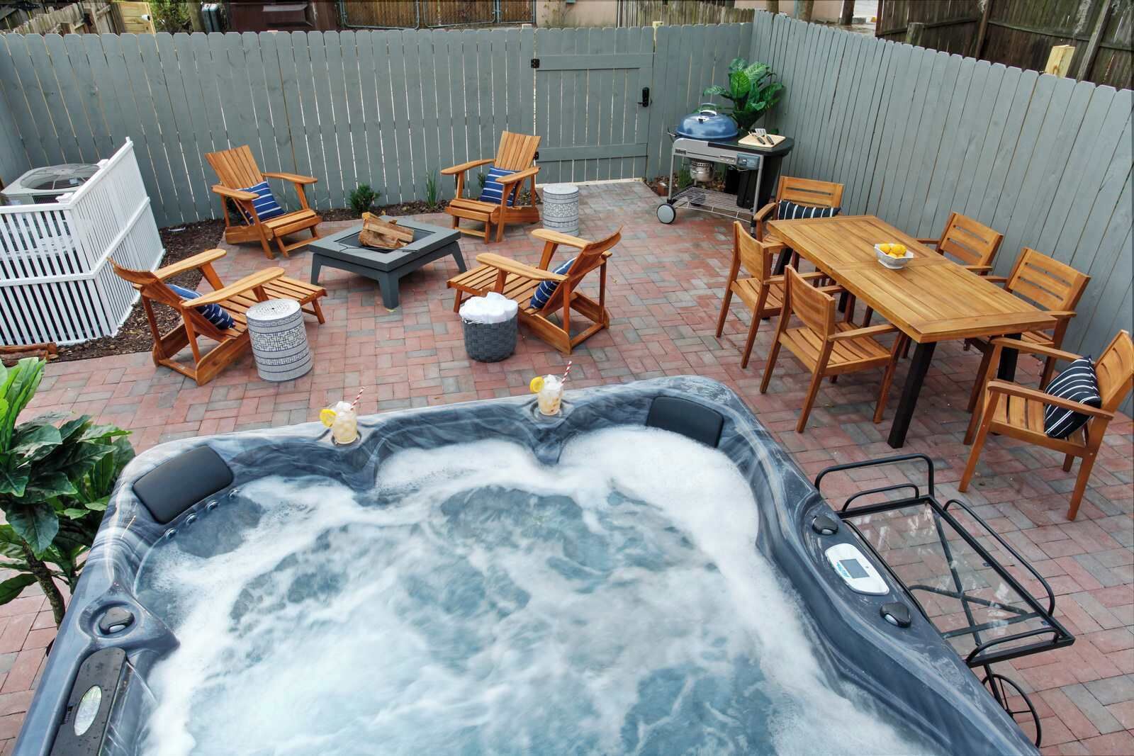Ein Garten mit Whirlpool, Holzstühlen, einem Tisch und einem Grill.
