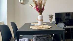 Un comedor moderno con una mesa rectangular, sillas negras y un florero blanco con plantas secas.