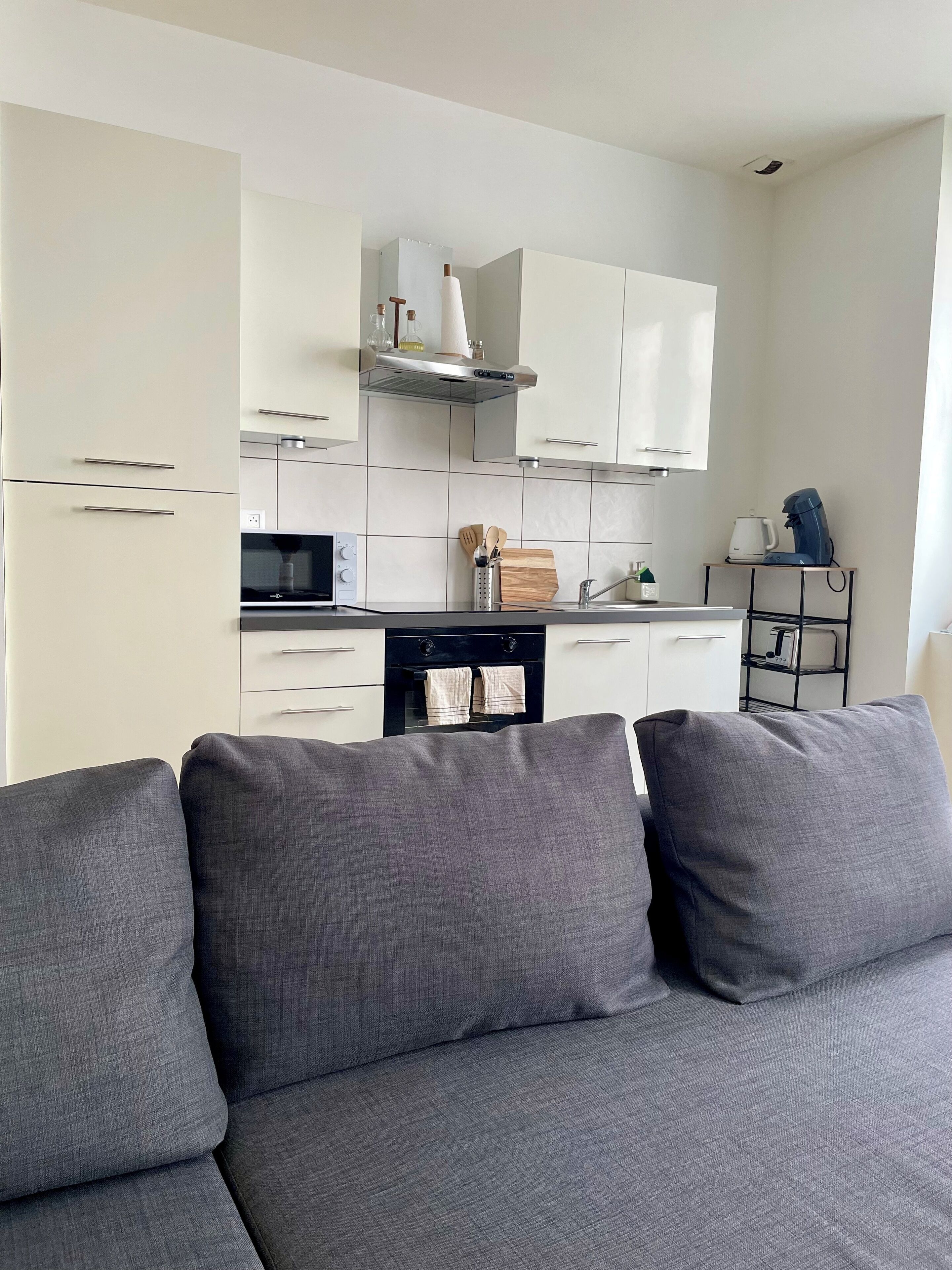 A modern kitchen with white cabinets, a stainless steel range hood, and a coffee machine.