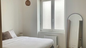 Un dormitorio con una cama, un tapete redondo, una silla de mimbre, un espejo y una ventana.