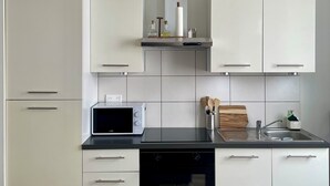 Una cocina moderna con armarios blancos, encimera negra, microondas, horno empotrado y pileta de acero inoxidable.