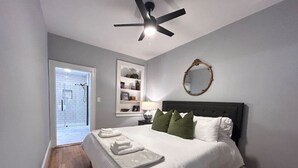 Een slaapkamer met een bed, een plafondventilator, een spiegel, een nachtkastje en een deur naar een balkon.