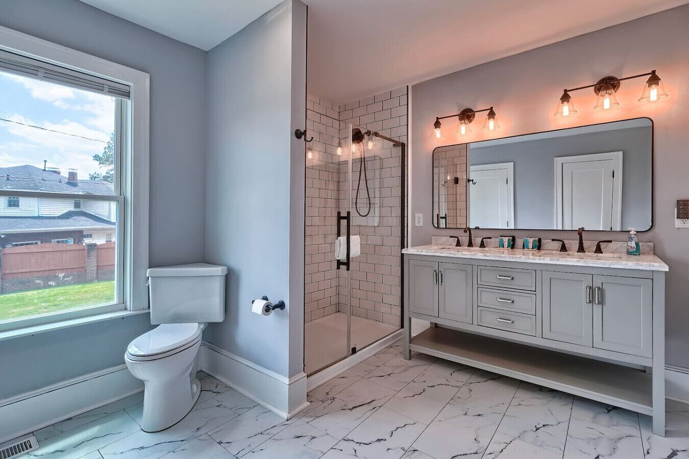 Un baño con inodoro, ducha con puertas de vidrio, tocador con espejo y ventana con vistas al exterior.