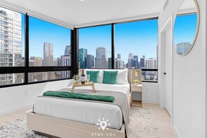 A modern bedroom with a large bed, a bedside table, a nightstand, a mirror, and a city view. - City Vibes with Spa & Gym in Sleek 1BR Retreat (Miami)