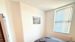 Une petite pièce, peu meublée, avec un lit simple, un radiateur et une fenêtre équipée de stores.