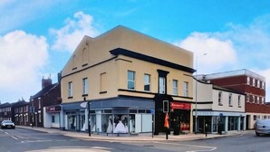 Un bâtiment à la façade moderne, une devanture avec une enseigne rouge et un carrefour en rotonde.