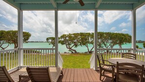 A covered outdoor area with a wooden deck, white railings, and a table with chairs. - Villa with Resort Amenities | Full Kitchen (Duck Key)