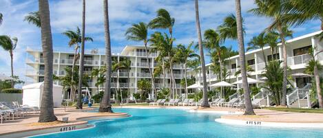 A resort with a swimming pool surrounded by palm trees and a multi-story building with balconies.