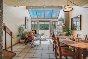 Een ruime woonkamer met een grote eettafel, comfortabele zithoek en uitzicht door een glazen deur op een bebost landschap.