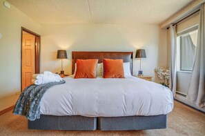Een hotelkamer met een groot bed, twee bedlampen, een deur en een raam met gordijnen.