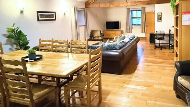 Ein geräumiger Wohnbereich mit einem Holzessttisch, mehreren Stühlen, einer Couch und einem Fernseher.