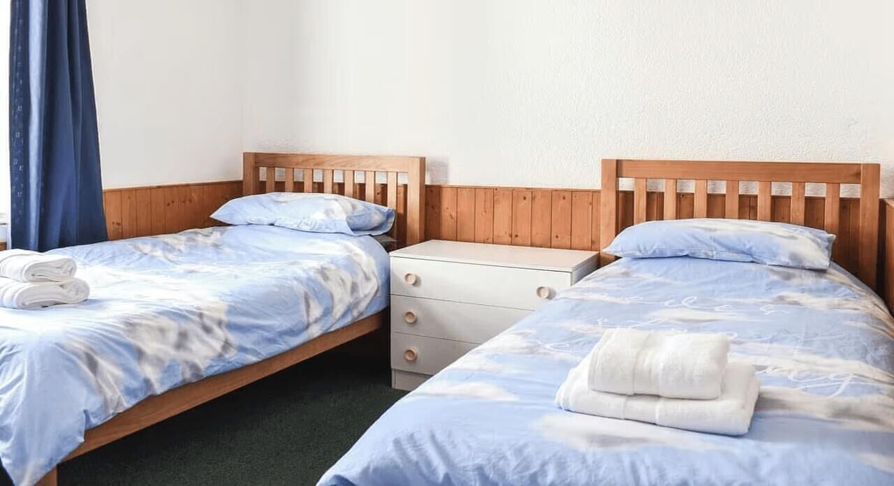 Ein Zimmer mit zwei Einzelbetten, jeweils mit einem Holz-Kopfteil, einem weißen Nachttisch und einer Schublade.
