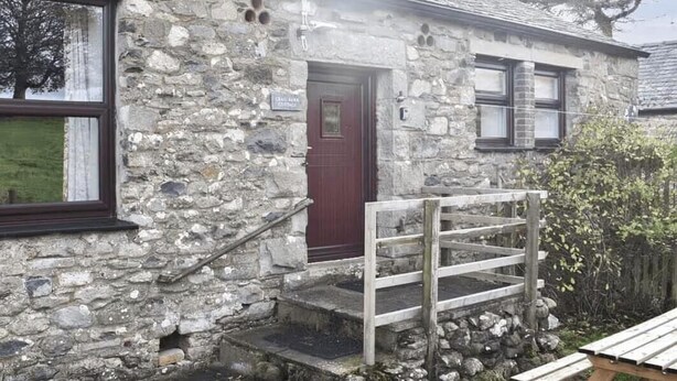 A stone building with a red door, a wooden gate, and a small set of steps leading to a wooden bench. - Crag Barn Cottage – Lake District Getaway by PolkaStays (Lake District)
