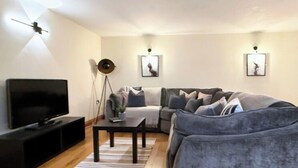 A modern living room with a grey sofa, a TV, a coffee table, and a dining table with chairs. - The Stables | Romantic Countryside Escape in the Lake District (Lake District)