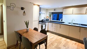 A modern kitchen with wooden flooring, a dining table with chairs, and a potted plant. - The Stables | Romantic Countryside Escape in the Lake District (Lake District)