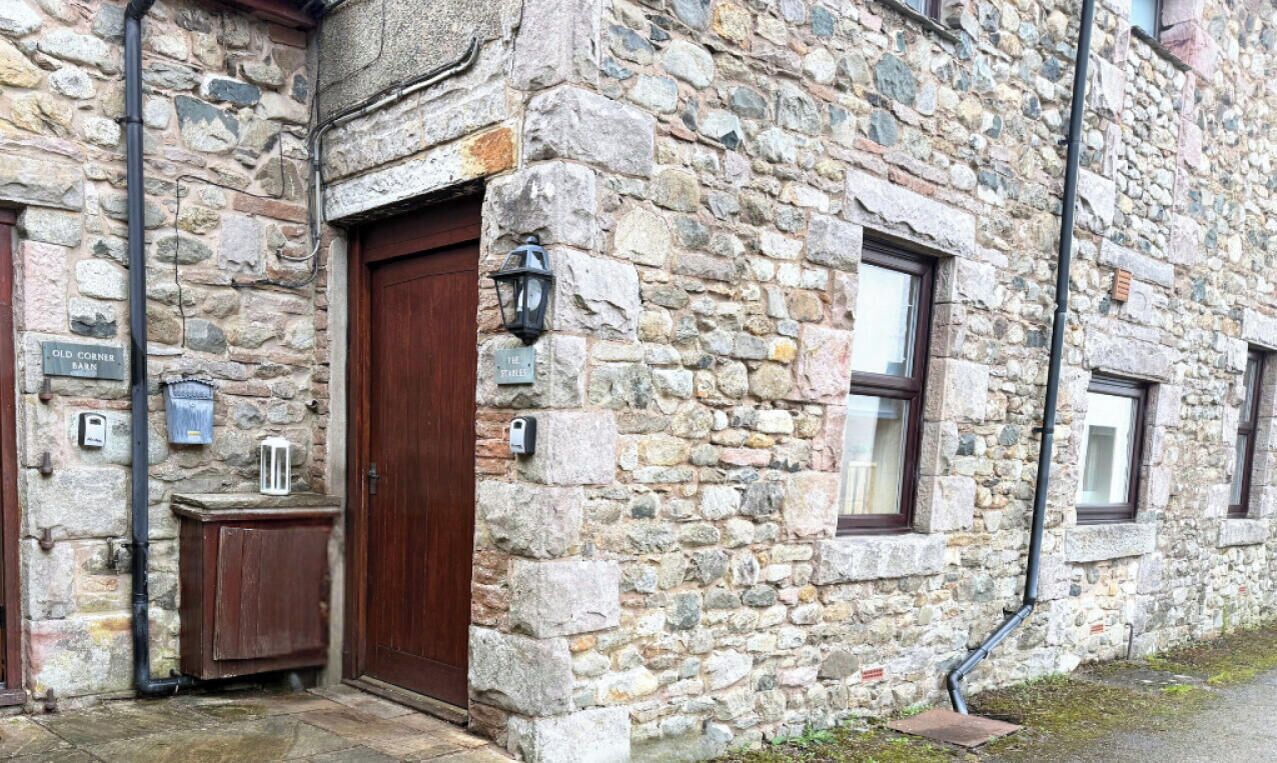 A stone building with a wooden door, a small cabinet, and a sign that reads "Old Corner Barn."