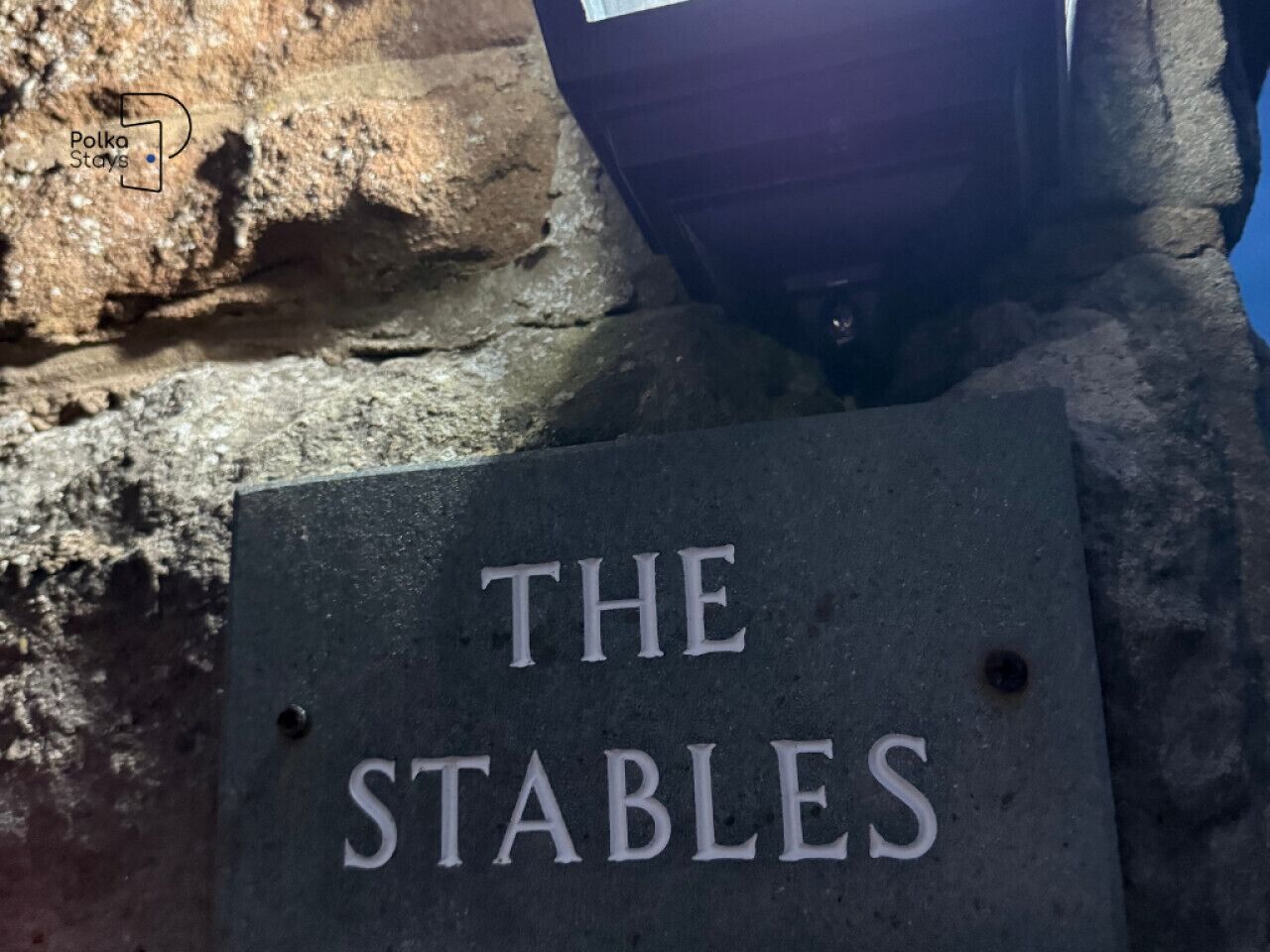 A sign with the text 'THE STABLES' on a stone surface.
