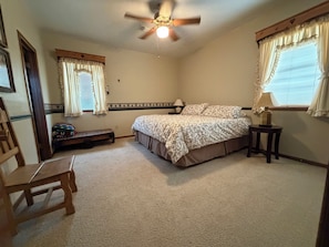 A bedroom with a bed, a ceiling fan, a nightstand, a lamp, and a bench.