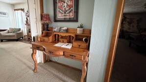 A wooden desk with drawers and a shelf, a framed poster on the wall, and a lamp.