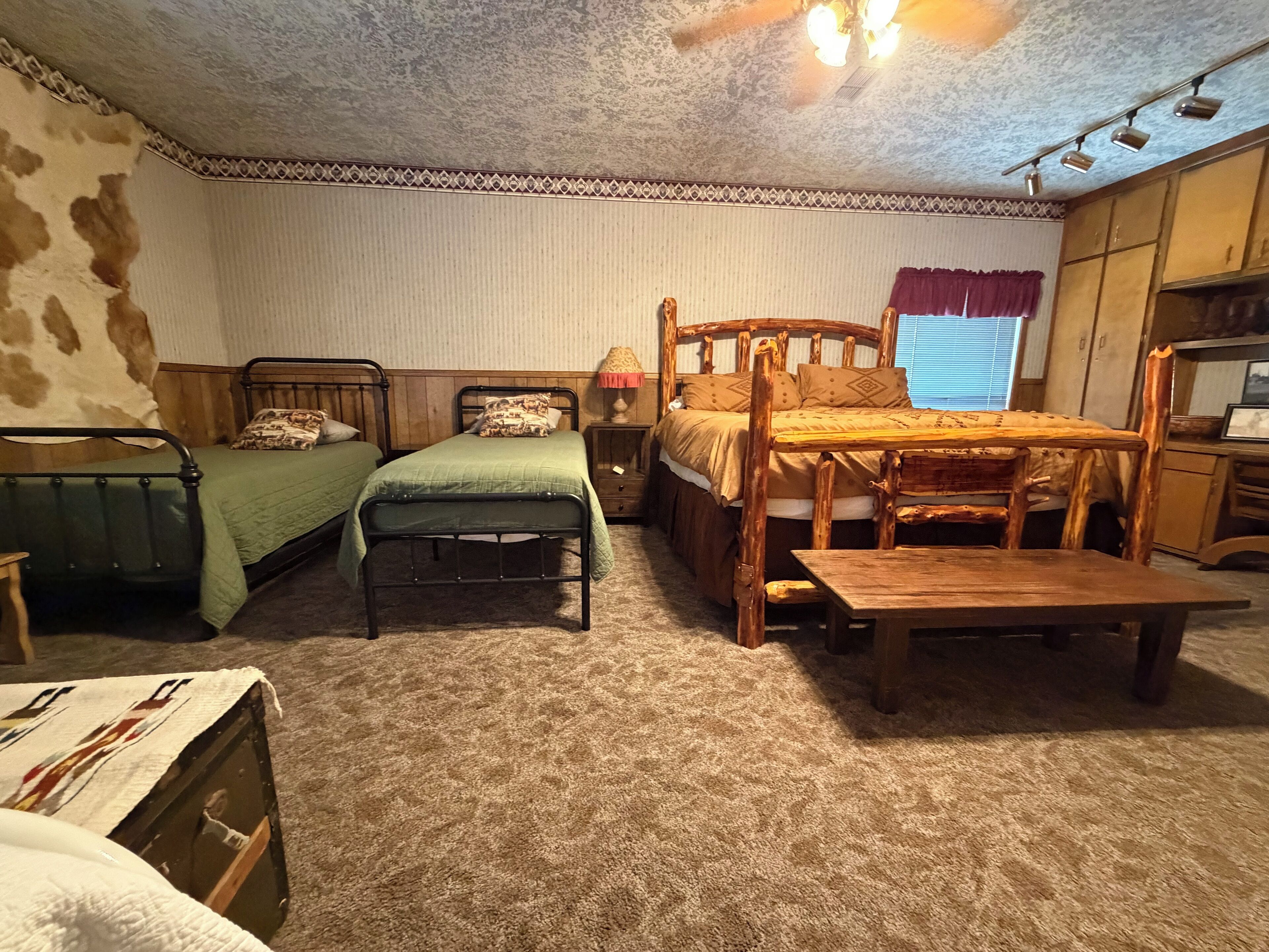 A room with two single beds, a wooden table, a small desk, and a window with curtains.