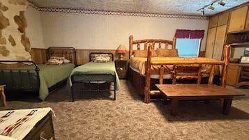A room with two single beds, a wooden table, a small desk, and a window with curtains.