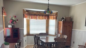 A dining area with a wooden table and chairs, a chandelier, and a window with blinds.