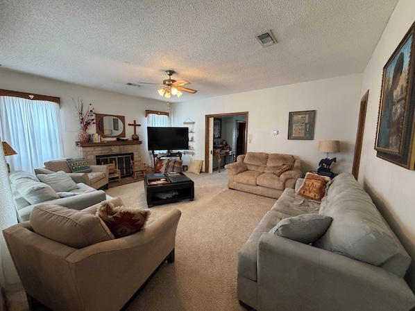 A living room with a fireplace, a television, and a ceiling fan.