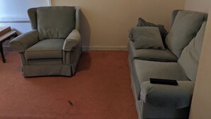Ein Wohnzimmer mit grauem Sessel und grauer Couch vor einer schlichten Wand.
