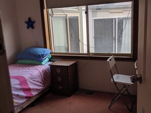 A bedroom with a single bed, a small dresser, a chair, and a window with a view of buildings outside. - Comfie House Clayton (Clayton South)