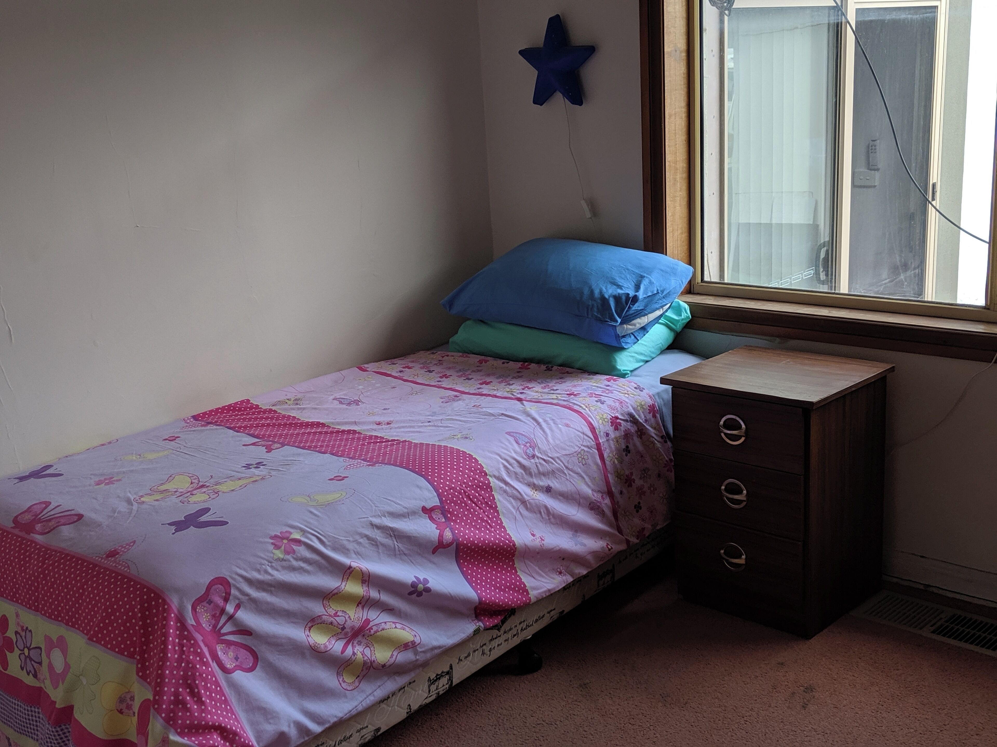 A small bedroom with a single bed, a dresser, and a window.