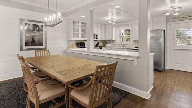 A modern kitchen with white cabinetry, a wooden dining table, and pendant lighting. - Large beach home w golf cart, minutes from beach! (St Simons Island)