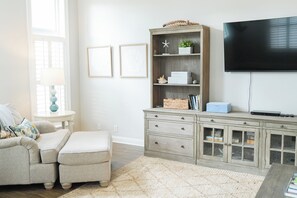 Een woonkamer met een bank, voetenbankje, houten kast, flatscreen televisie en een tafeltje met een lamp.