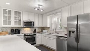 A modern kitchen with white cabinets, stainless steel appliances, and a large island. - Large beach home w golf cart, minutes from beach! (St Simons Island)