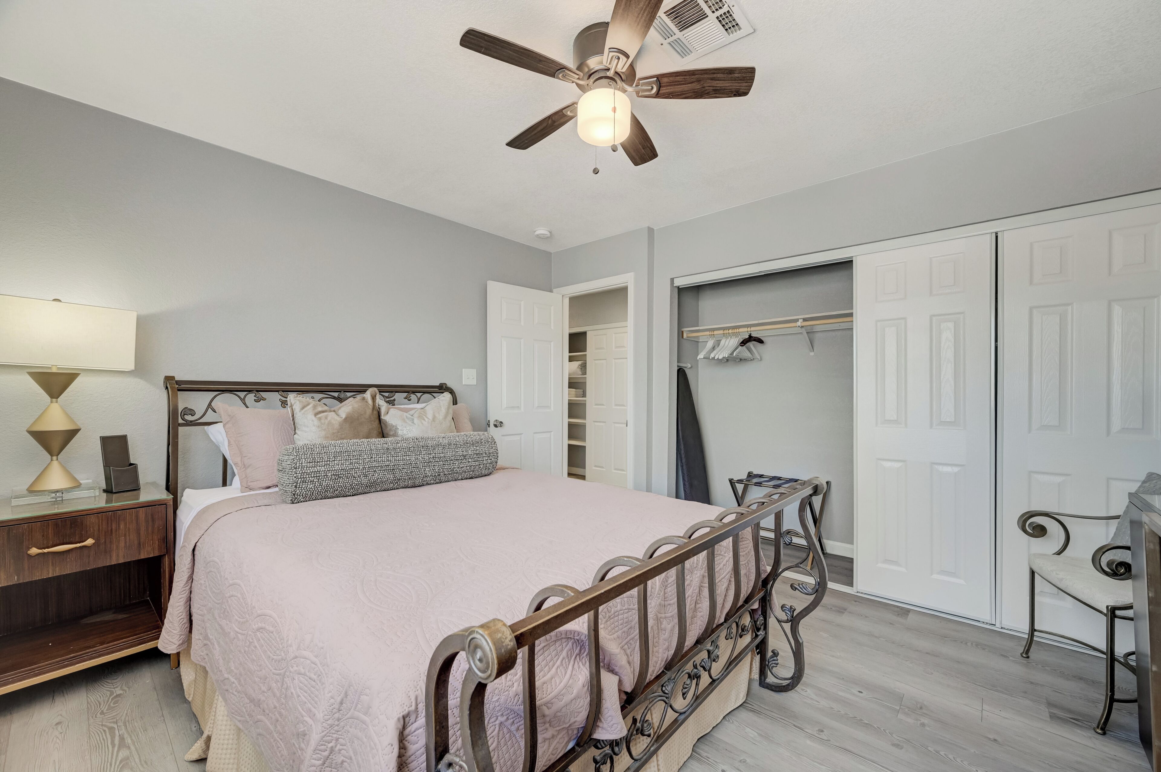 A bedroom with a bed, bedside table, lamp, wardrobe, and ceiling fan.