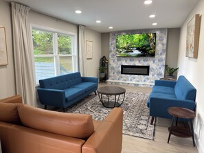 Una sala de estar con un sofá azul, un sofá de cuero marrón, un televisor montado en una pared de piedra y una chimenea.