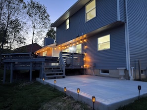 Una casa de dos pisos con terraza, iluminación exterior y un porche cubierto.