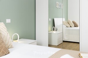 A bedroom with a bed, bedside table, and a nightstand with a lamp. - Green Modern Apartment (Monserrato)