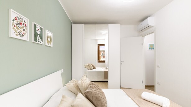 Une chambre à coucher avec un lit, des oreillers, une table de chevet et un climatiseur fixé au mur.