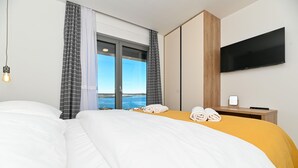 Une chambre d’hôtel avec un grand lit, un téléviseur fixé au mur et une vue sur la mer par la fenêtre.